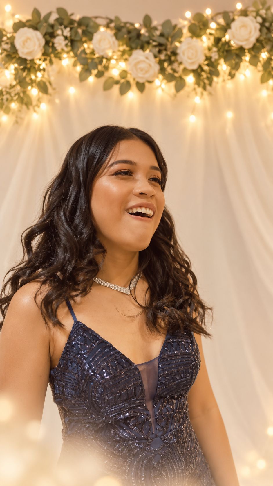 Angels laughing, in a navy sequinned gown beneath a garland of white roses and fairy lights